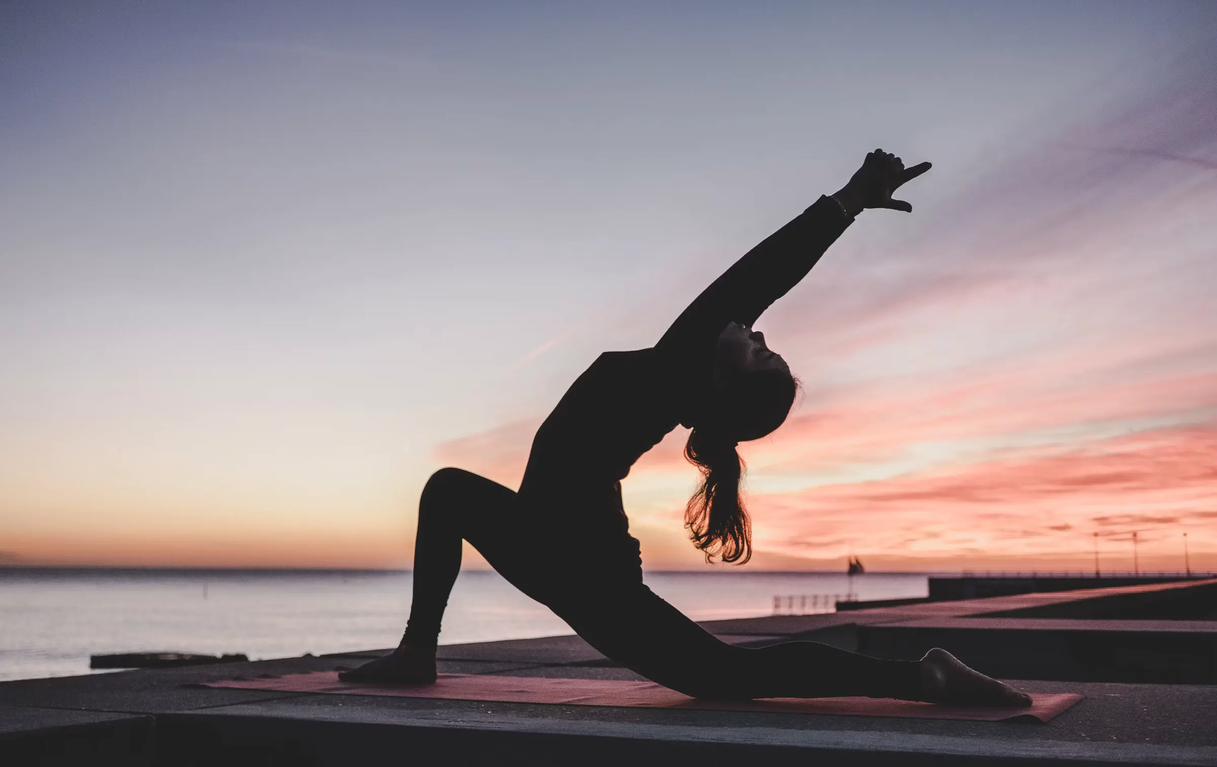 Woman doing yoga by the sea at sunset